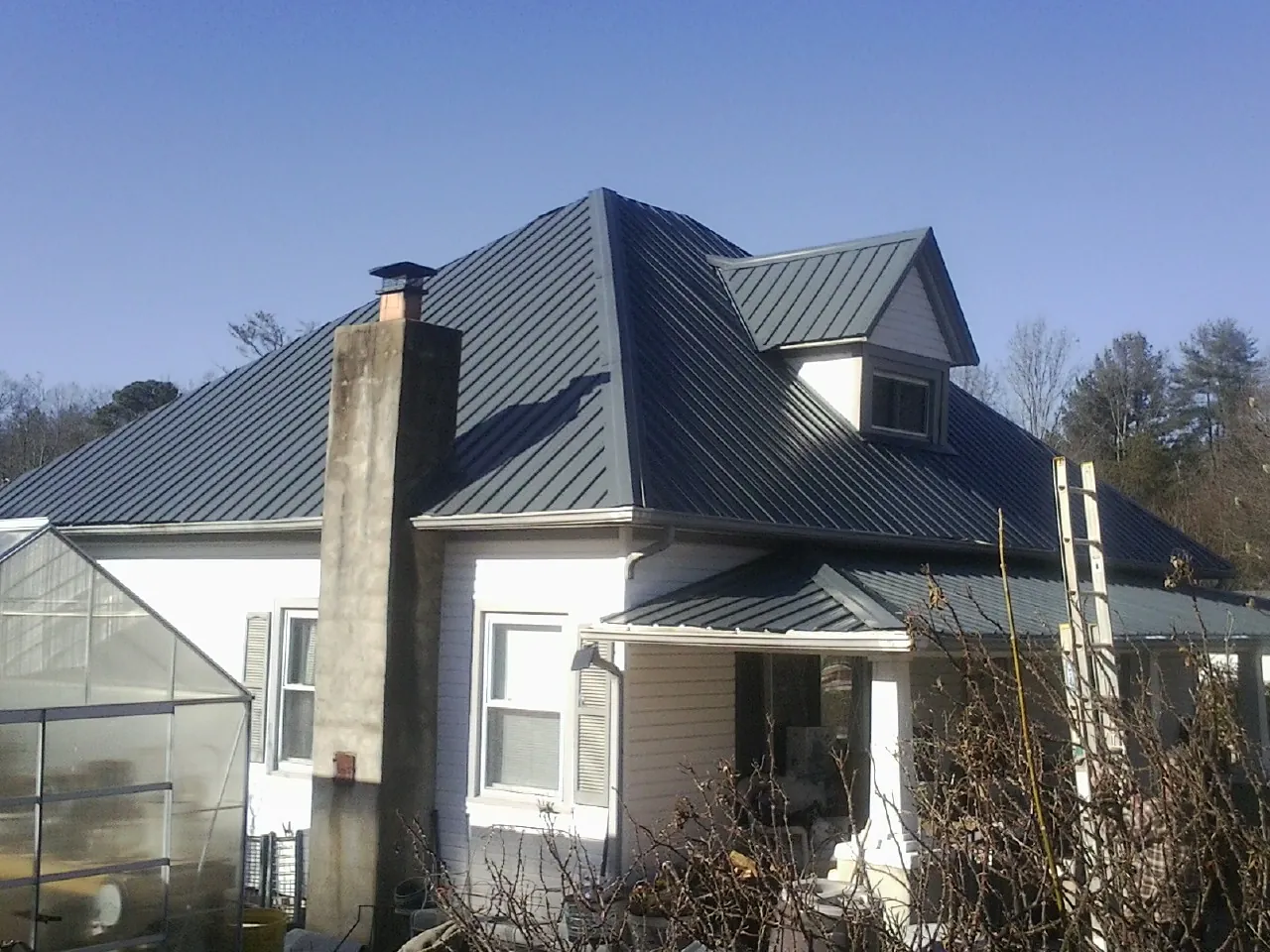 Dark blue standing seam metal roof on a white farmhouse with dormer — Slate & Tile Roof Repair by Roofing Brothers in Grasston