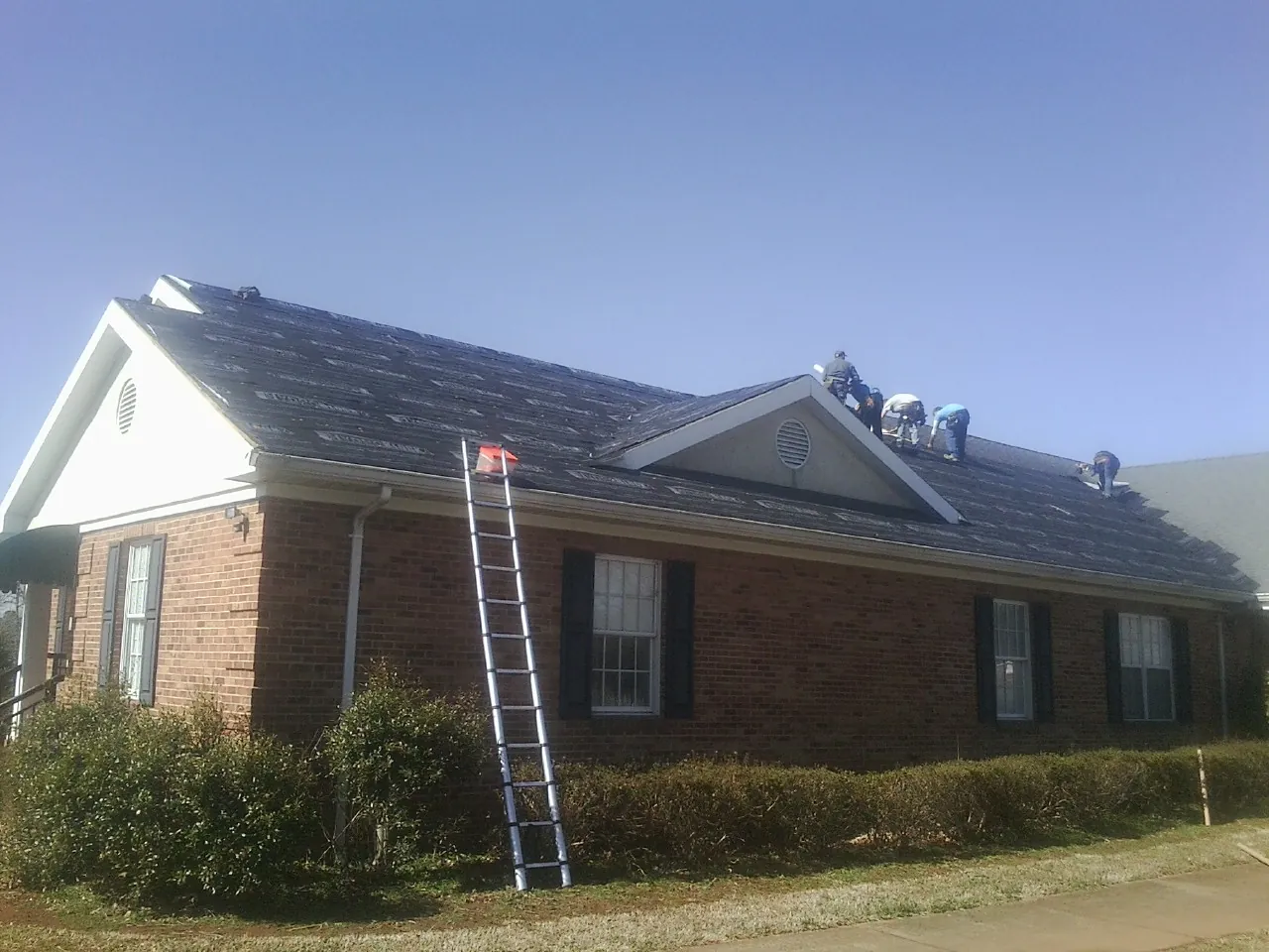 Crew tearing shingles off a brick ranch roof with a ladder set — Emergency Roof Repair work by our crew in Grasston