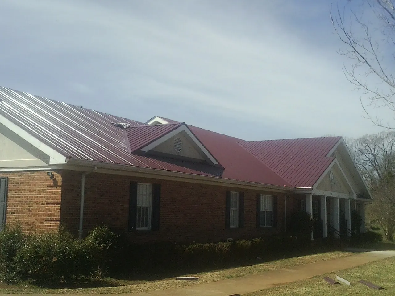 Red metal roof with gabled entries on a long brick building, from a Hail Damage Roof Repair job in Grasston