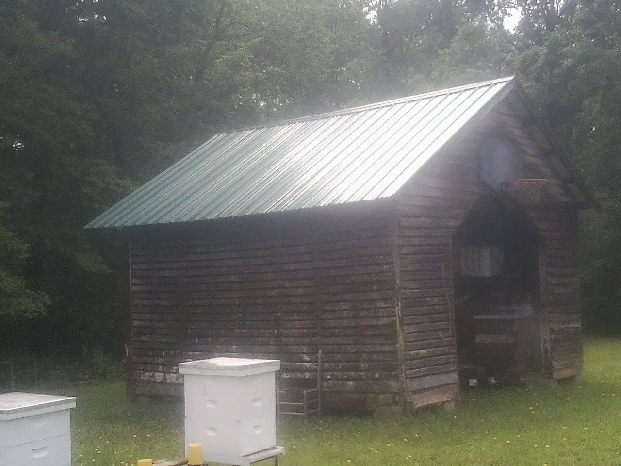Green metal roof on a weathered barn beside stacked beehives in Grasston