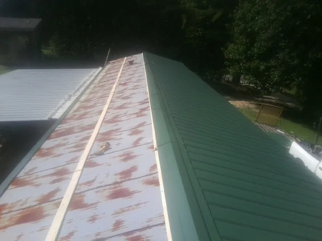 Old rusted panels beside newly installed green metal roofing — Wind Damage Roof Repair by Roofing Brothers in Grasston